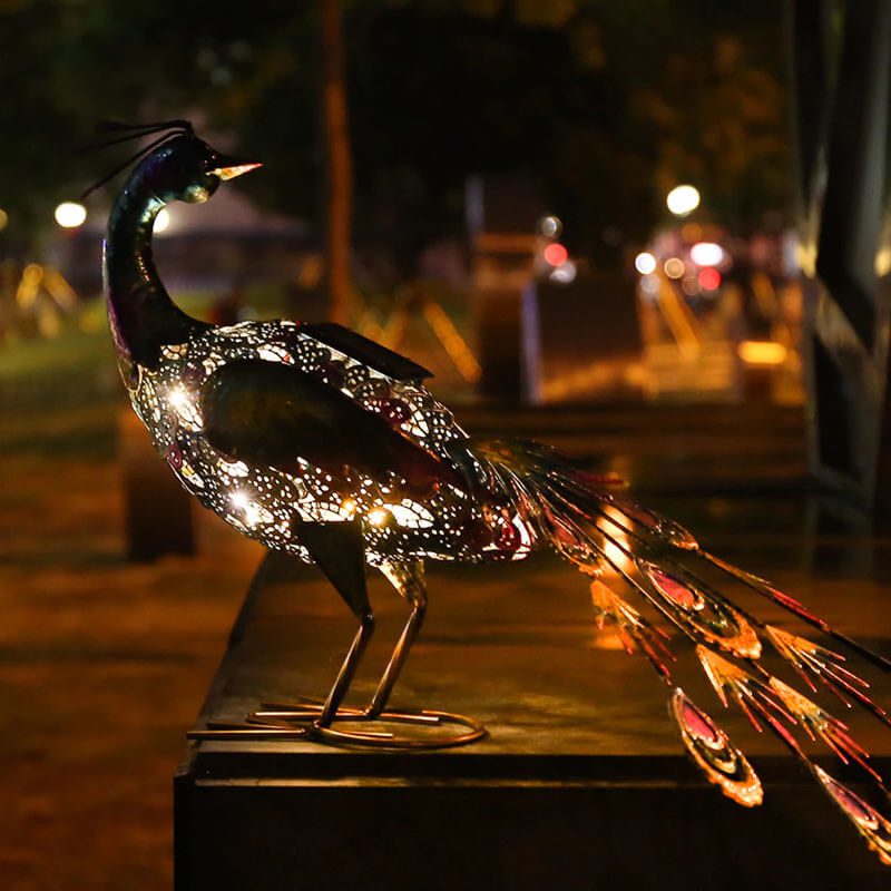 Décoration solaire paon en métal installée dans un jardin